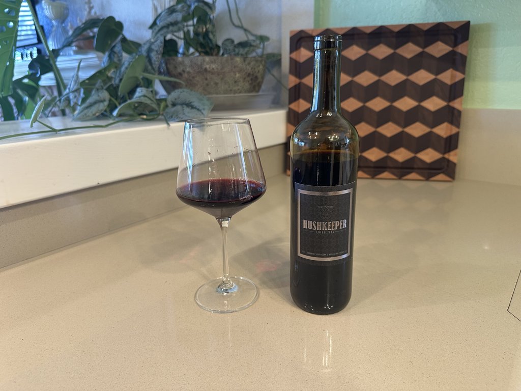 Bottle of 2022 Hushkeeper Cabernet Sauvignon next to a glass of red wine